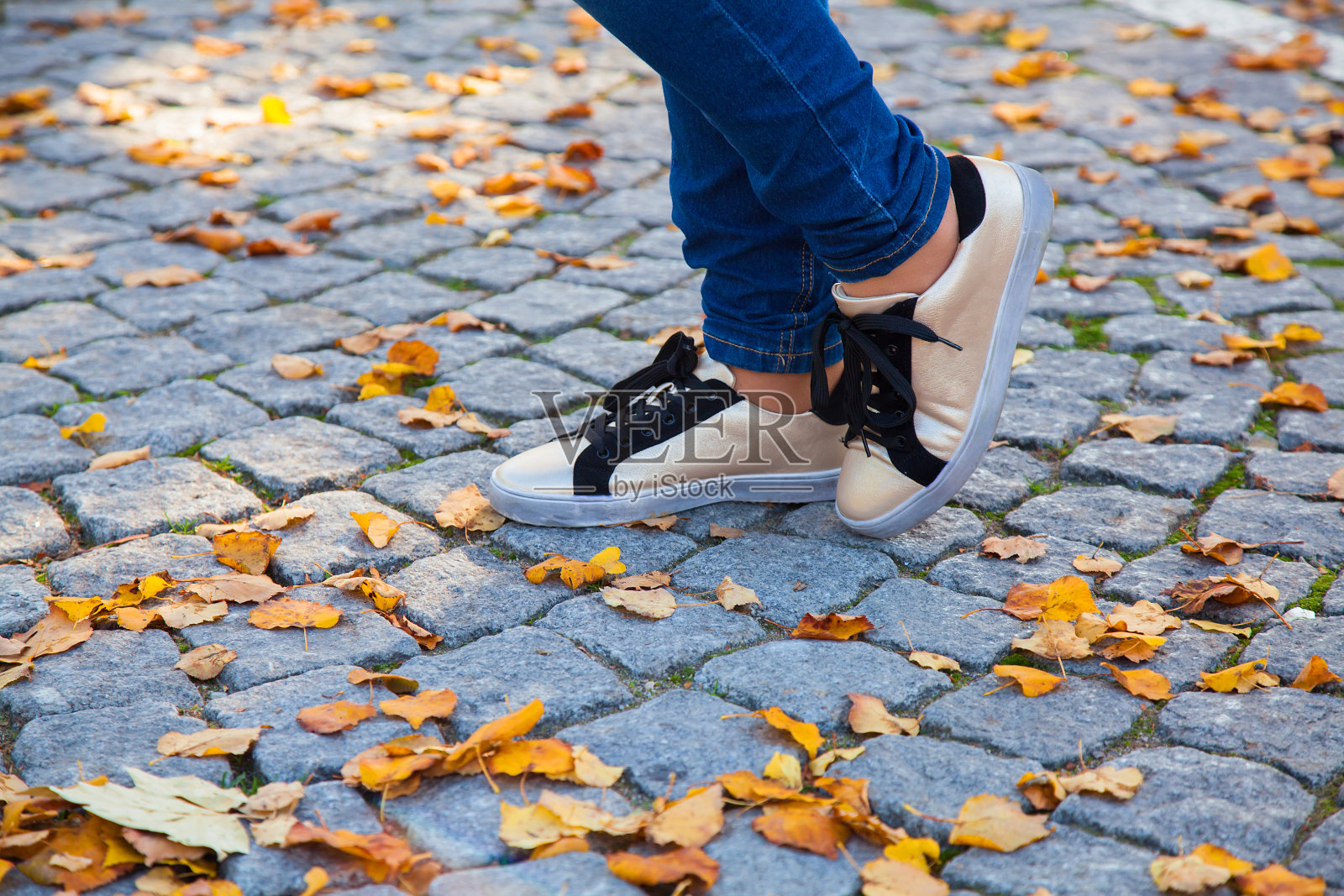 在秋天金色树叶上的牛仔裤和运动鞋的脚的特写照片摄影图片