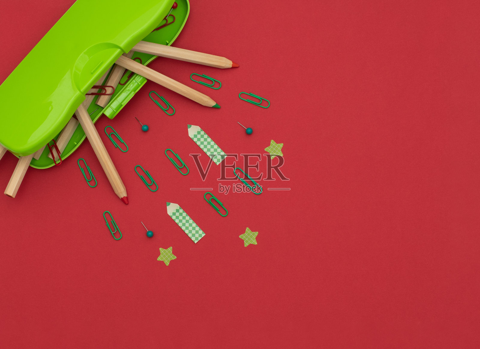 绿色铅笔盒，木制铅笔，红色和绿色的回形针和别针，铅笔和星星形状的纸贴纸在红色的背景。学校和办公用品，文具。回到学校的概念。平躺风格照片摄影图片