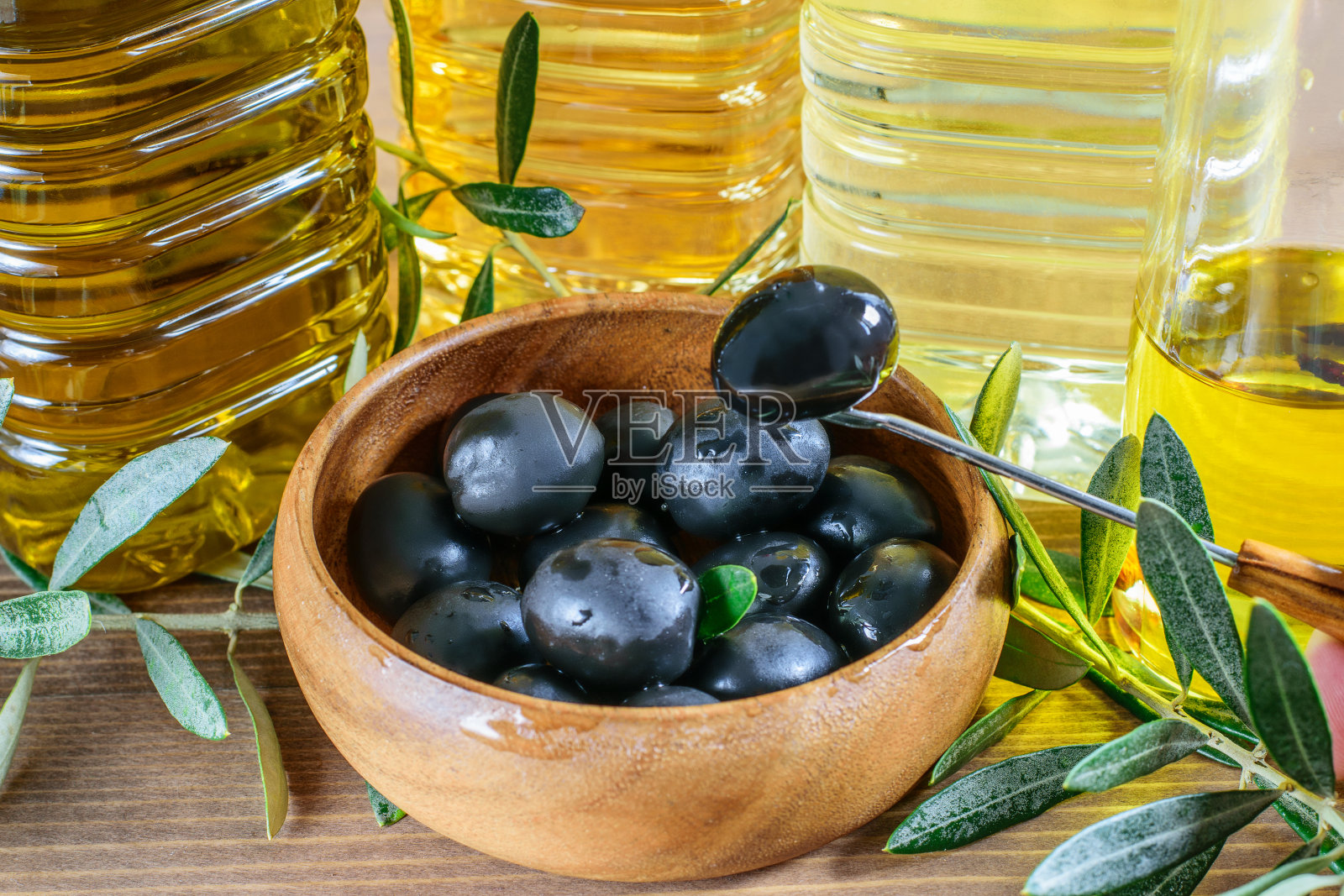 木碗里的新鲜黑橄榄。橄榄树的树枝，以及各种各样的橄榄油在木头上特写。健康饮食，地中海饮食。照片摄影图片