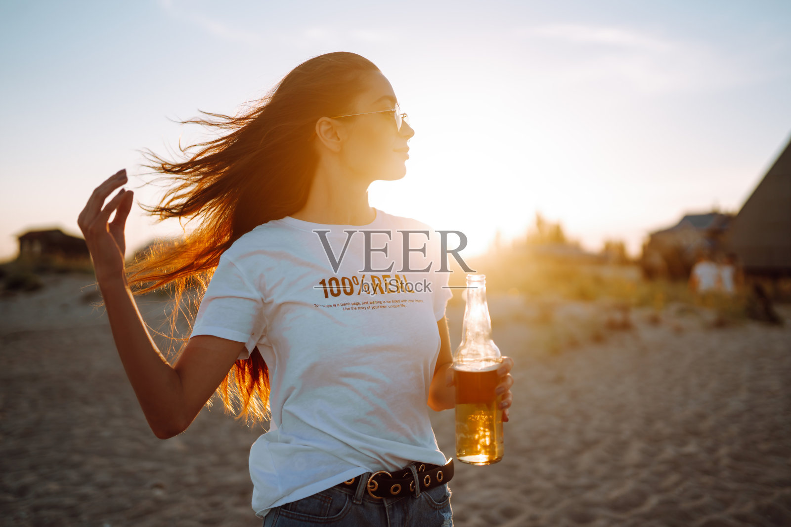 日落时分在海滩上喝啤酒的漂亮女孩。照片摄影图片