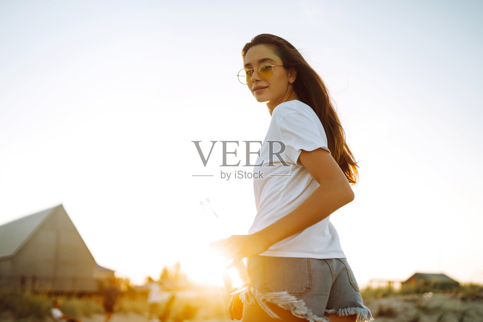 日落时分在海滩上喝啤酒的漂亮女孩。照片摄影图片