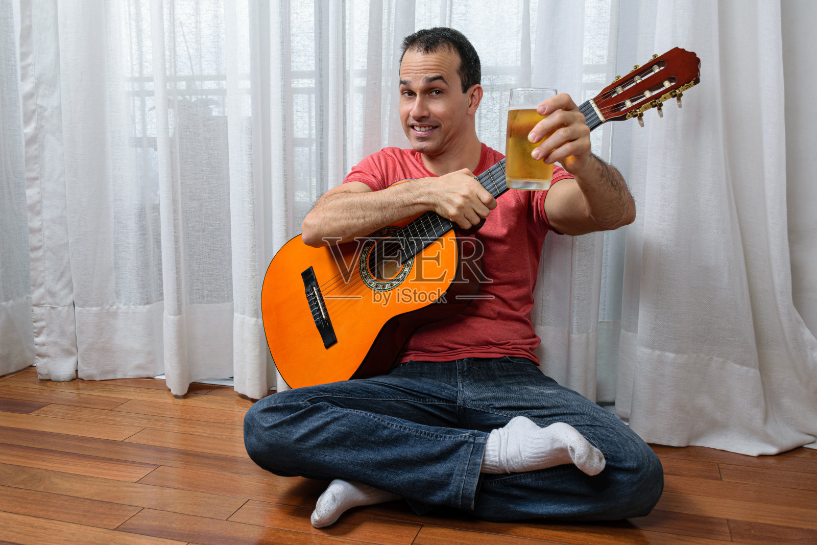微笑的成熟男子(44岁)，腿上放着吉他，递着一杯啤酒。照片摄影图片