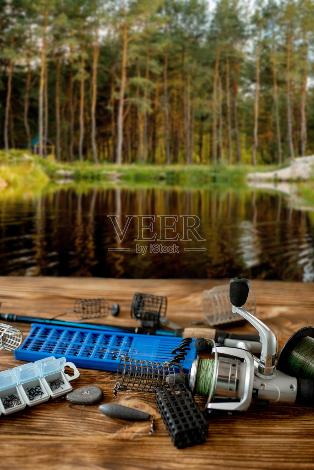 渔具及配件放在桌子上，背景是一个森林湖。有选择性的重点照片摄影图片