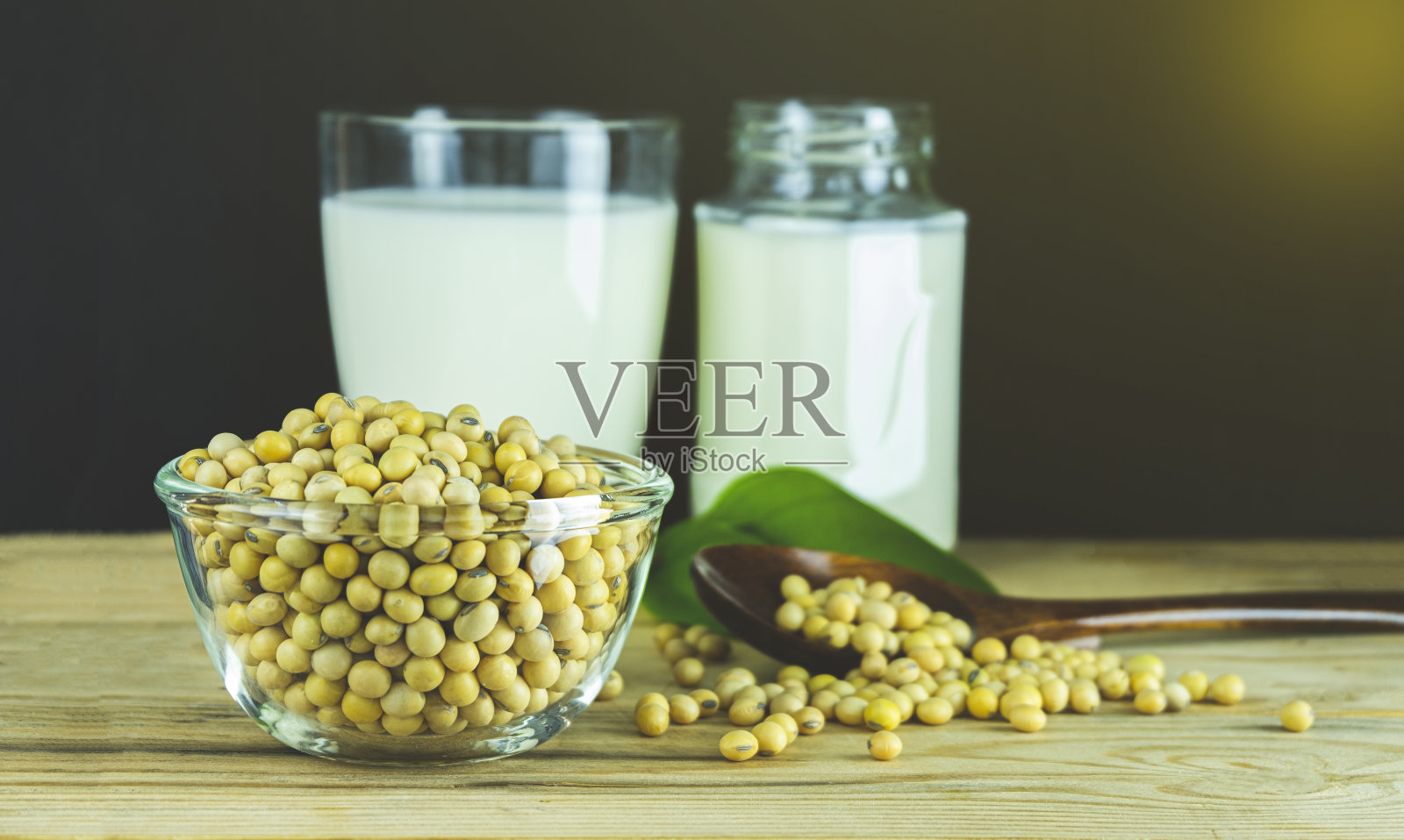 一杯豆浆，勺子上放着豆籽。照片摄影图片