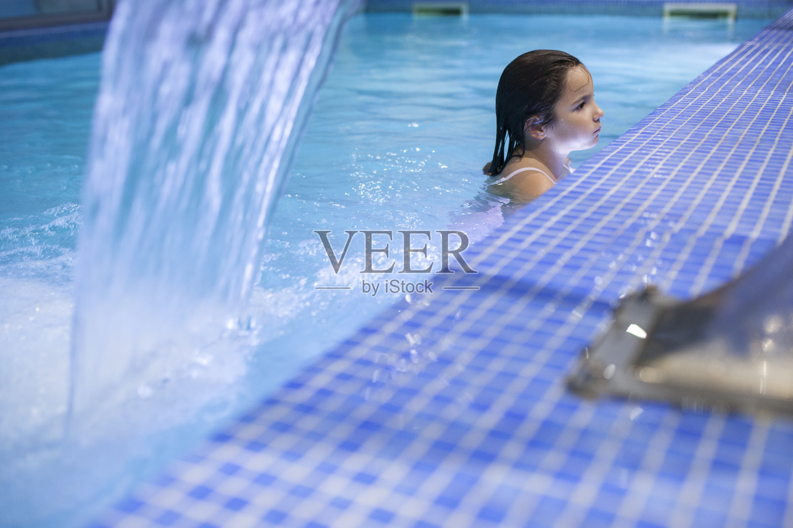 7岁的小女孩在室内游泳池享受瀑布喷射水疗照片摄影图片