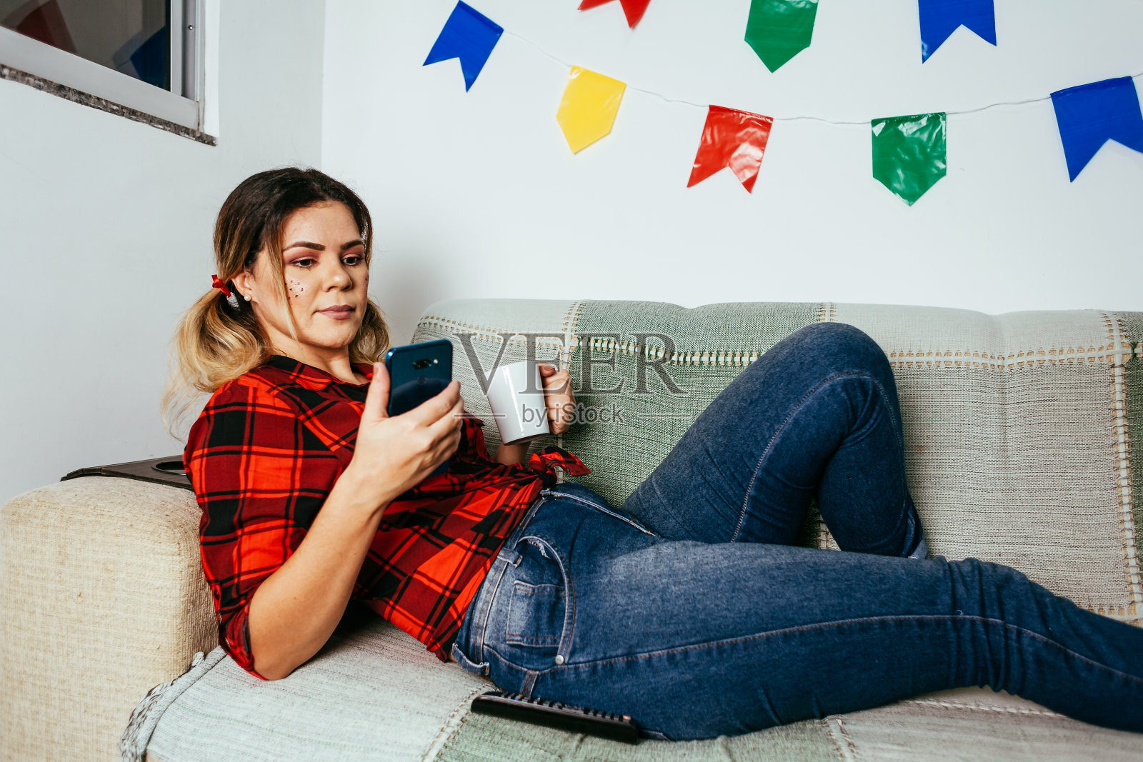 巴西节日朱尼纳在家。穿着典型服装的人。客厅装饰着彩旗。女人使用手机。照片摄影图片