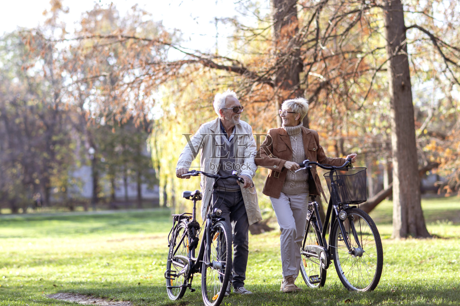 一对成熟的情侣在公园里推着自行车谈笑风生照片摄影图片
