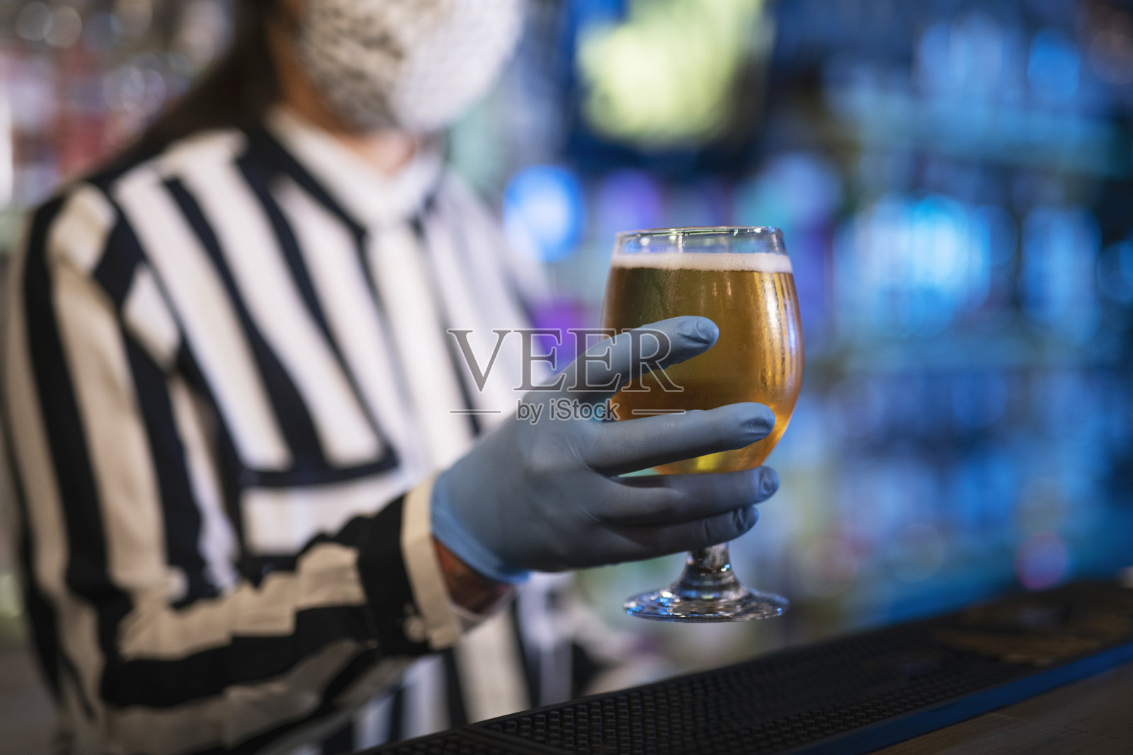 戴着防护面具和手术手套的女酒保端上啤酒。照片摄影图片