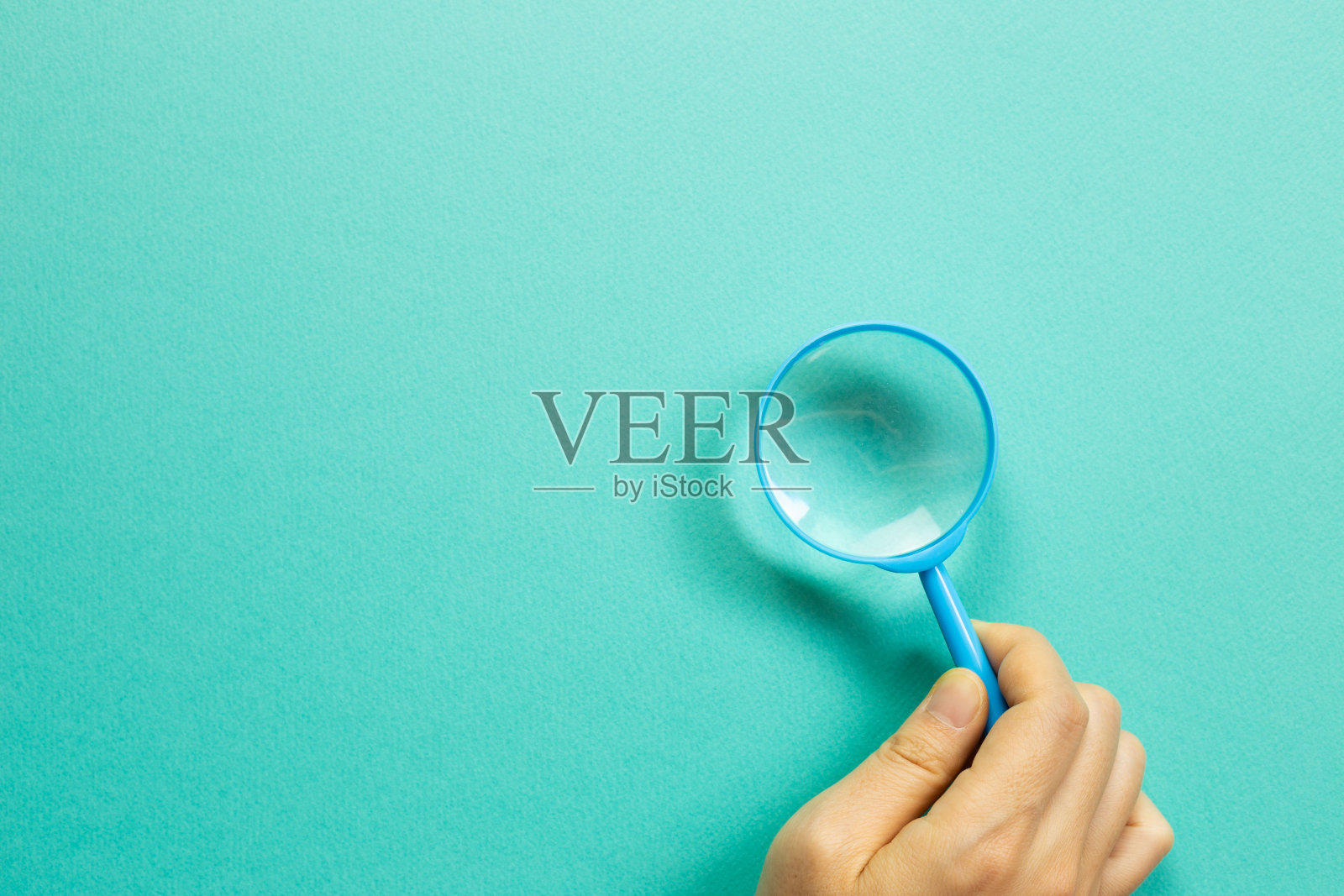 手拿蓝色放大镜在绿色背景。俯视图，复制空间照片摄影图片