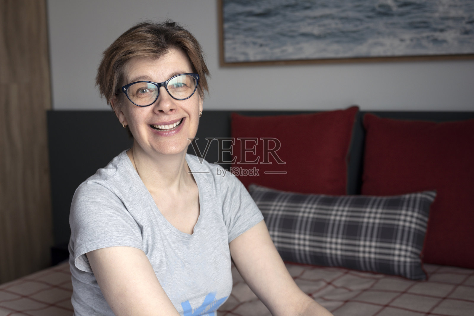 一个微笑的，快乐的，50岁妇女的肖像。坐在家里卧室的床上。照片摄影图片