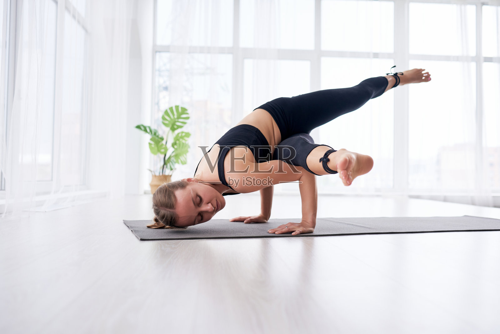 年轻漂亮的女人在一个现代明亮的房间里做瑜伽，房间里有大窗户。瑜伽在家的概念。照片摄影图片