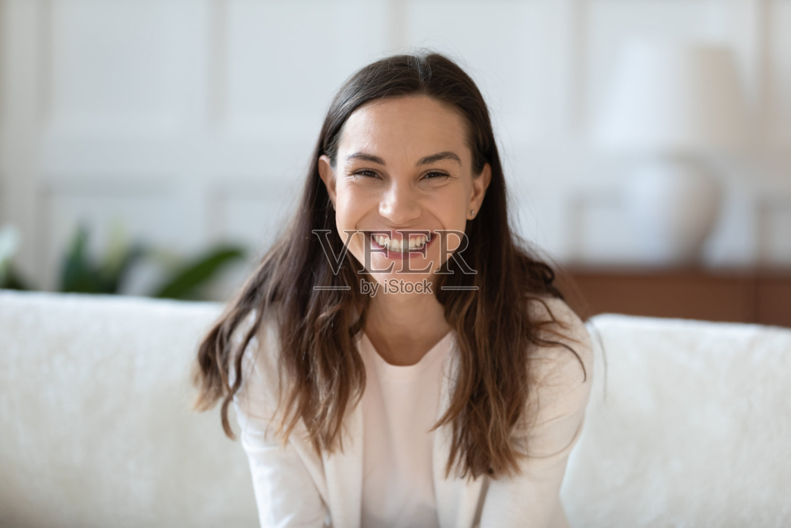 微笑的年轻女子坐在家里的沙发上的肖像照片摄影图片
