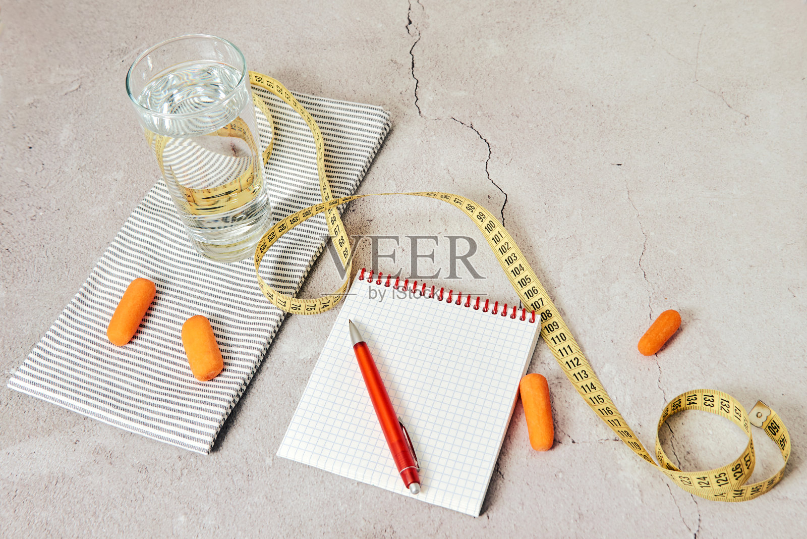 减肥、瘦身和节食的概念——一杯水，脱衣餐巾，黄色的卷尺，胡萝卜，笔记本，红色的钢笔都放在大理石做的桌子上照片摄影图片