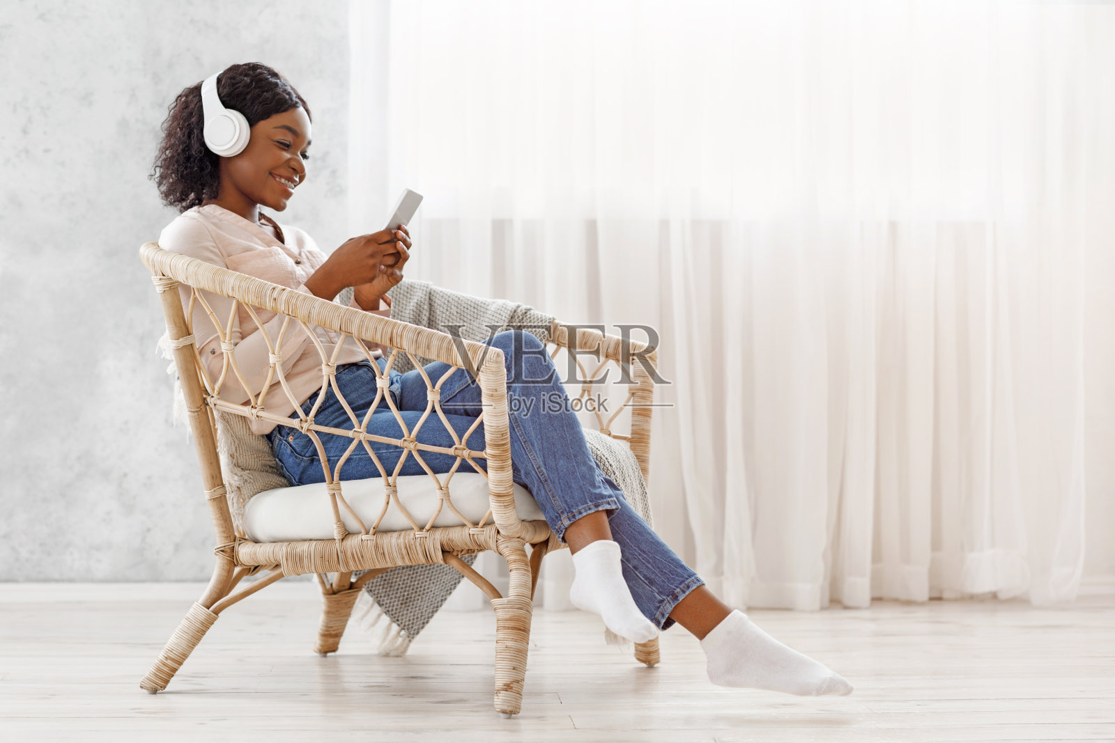 周末放松。美丽的黑人女孩在扶手椅上放松，在智能手机上听音乐照片摄影图片