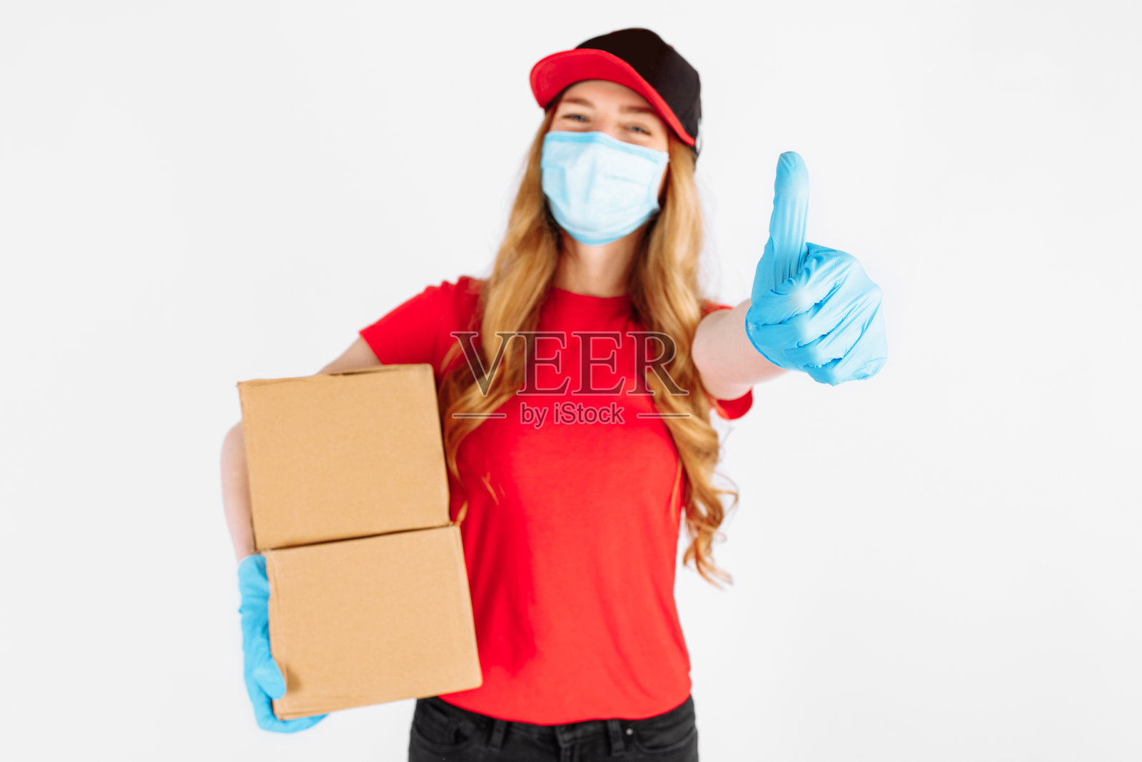 信使戴着医用橡胶手套和医用口罩，拿着纸盒，在白色背景下竖起大拇指。银行转账支付，冠状病毒照片摄影图片