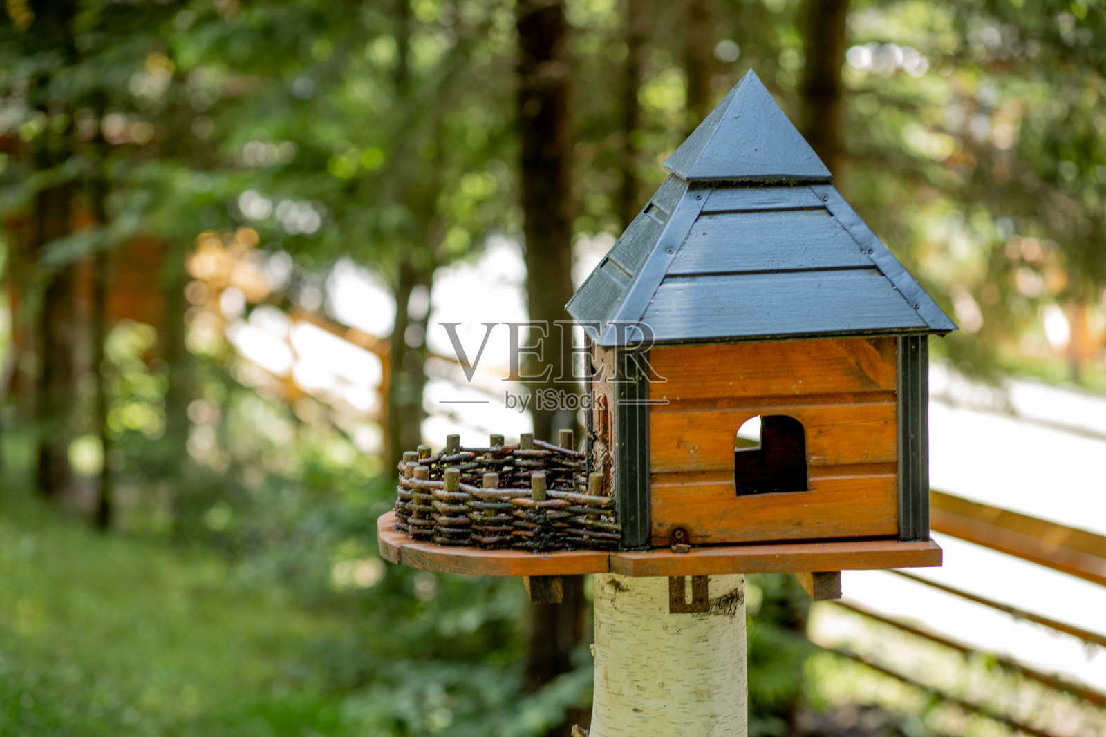 木制的鸟食器是一间带屋顶的房子，附着在一根木柱上，置身于大自然的树林之中照片摄影图片