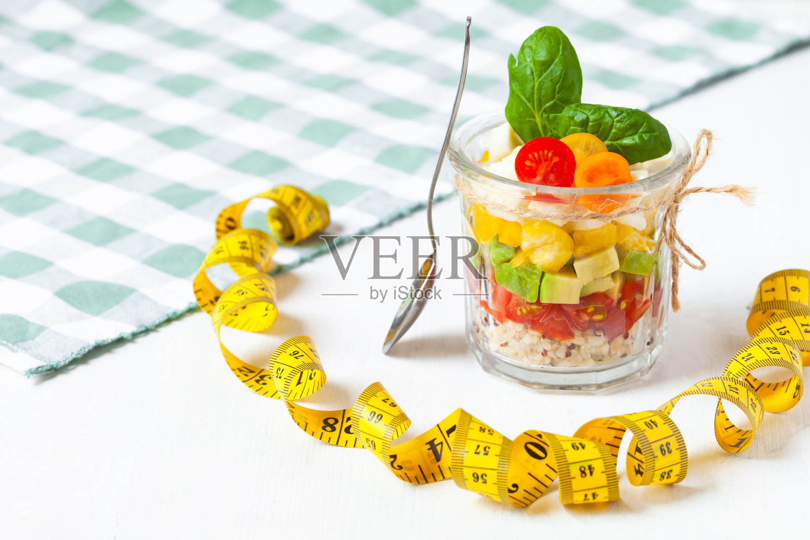 健康食品的理念，干净的饮食，低热量的美味佳肴。藜麦沙拉和新鲜蔬菜，橄榄油在玻璃罐中。卷尺测量，零浪费无塑料。特写白色背景照片摄影图片