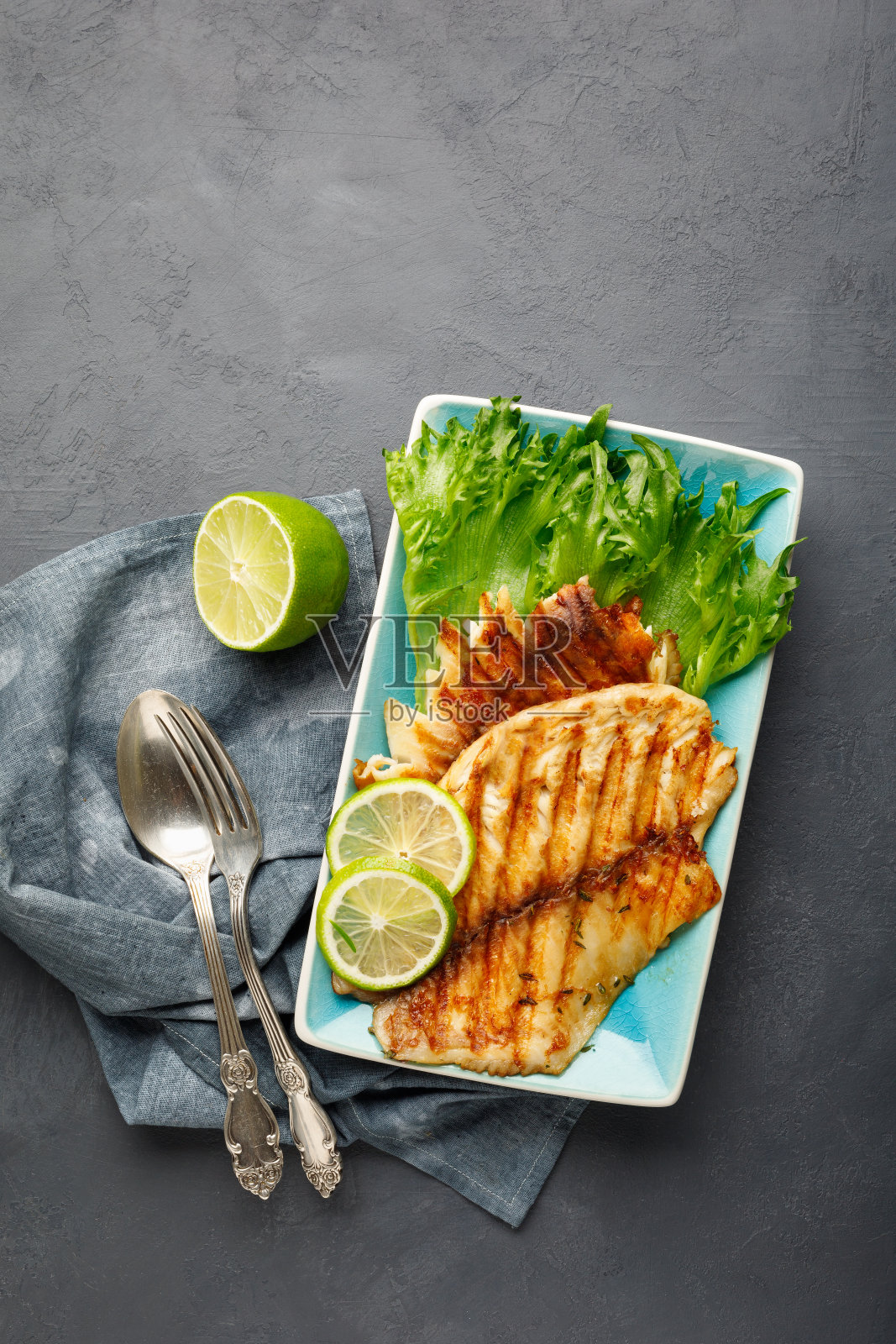 烤鱼配新鲜的香草和酸橙放在长方形的蓝色盘子里。照片摄影图片