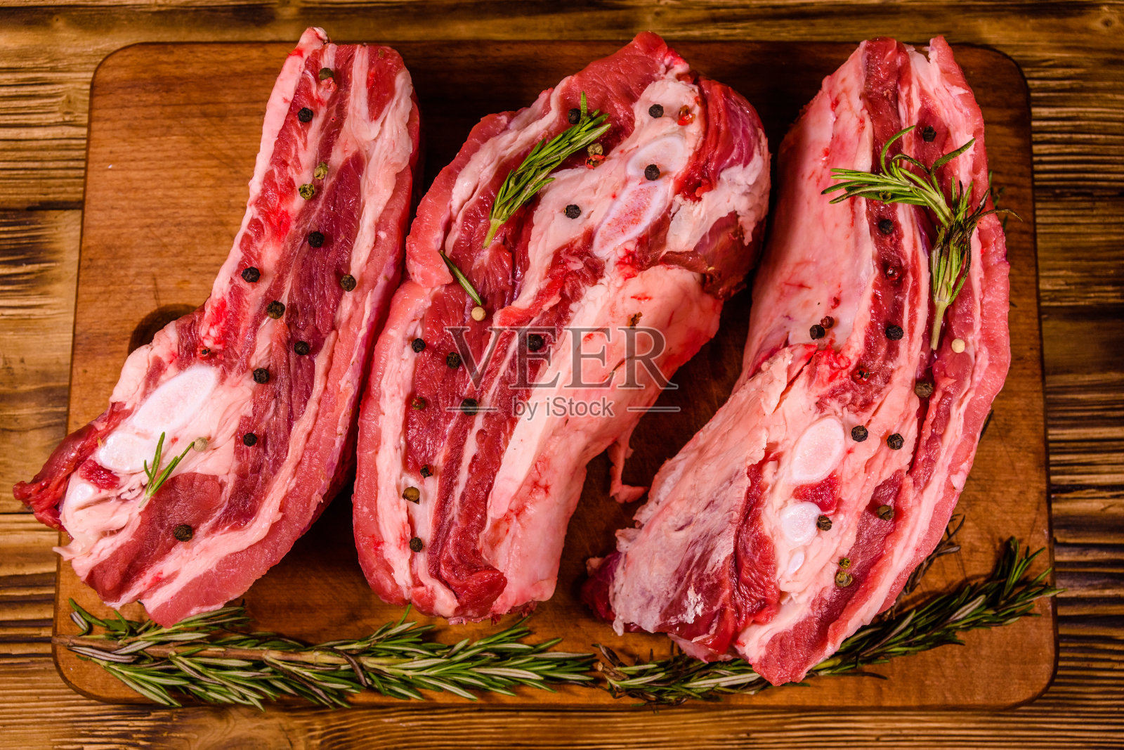 在切菜板上放上香料和迷迭香的生排骨。俯视图照片摄影图片