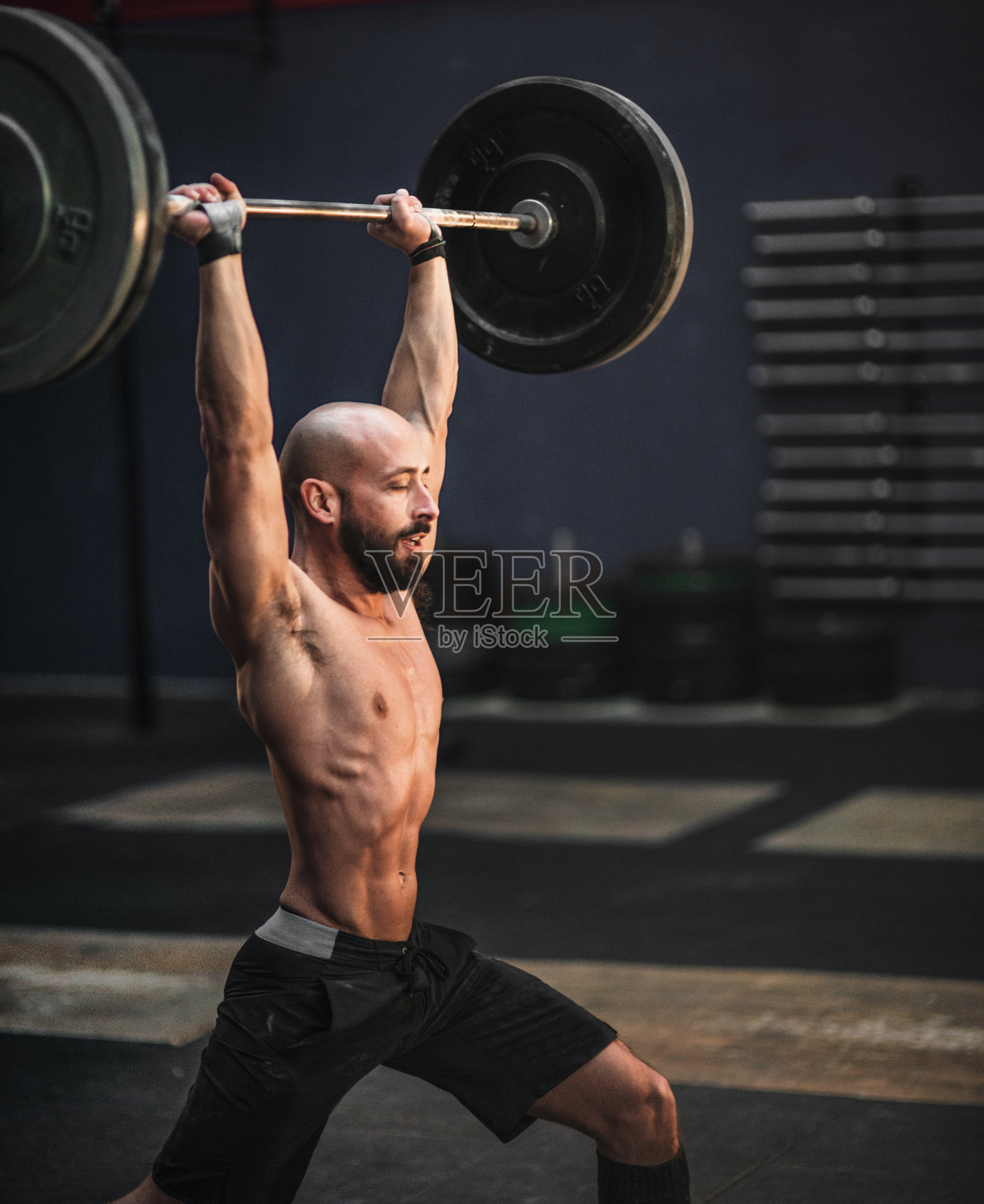 冠状病毒感染期间，秃头男子在健身房举重照片摄影图片