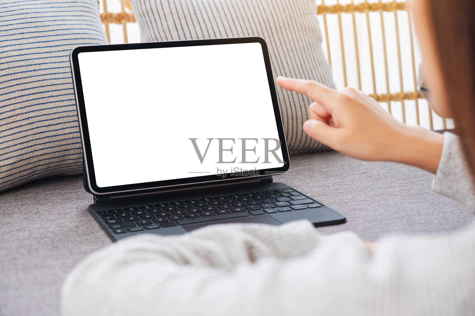 一个女人在家里的沙发上用手指着空白的桌面白色屏幕的平板电脑照片摄影图片