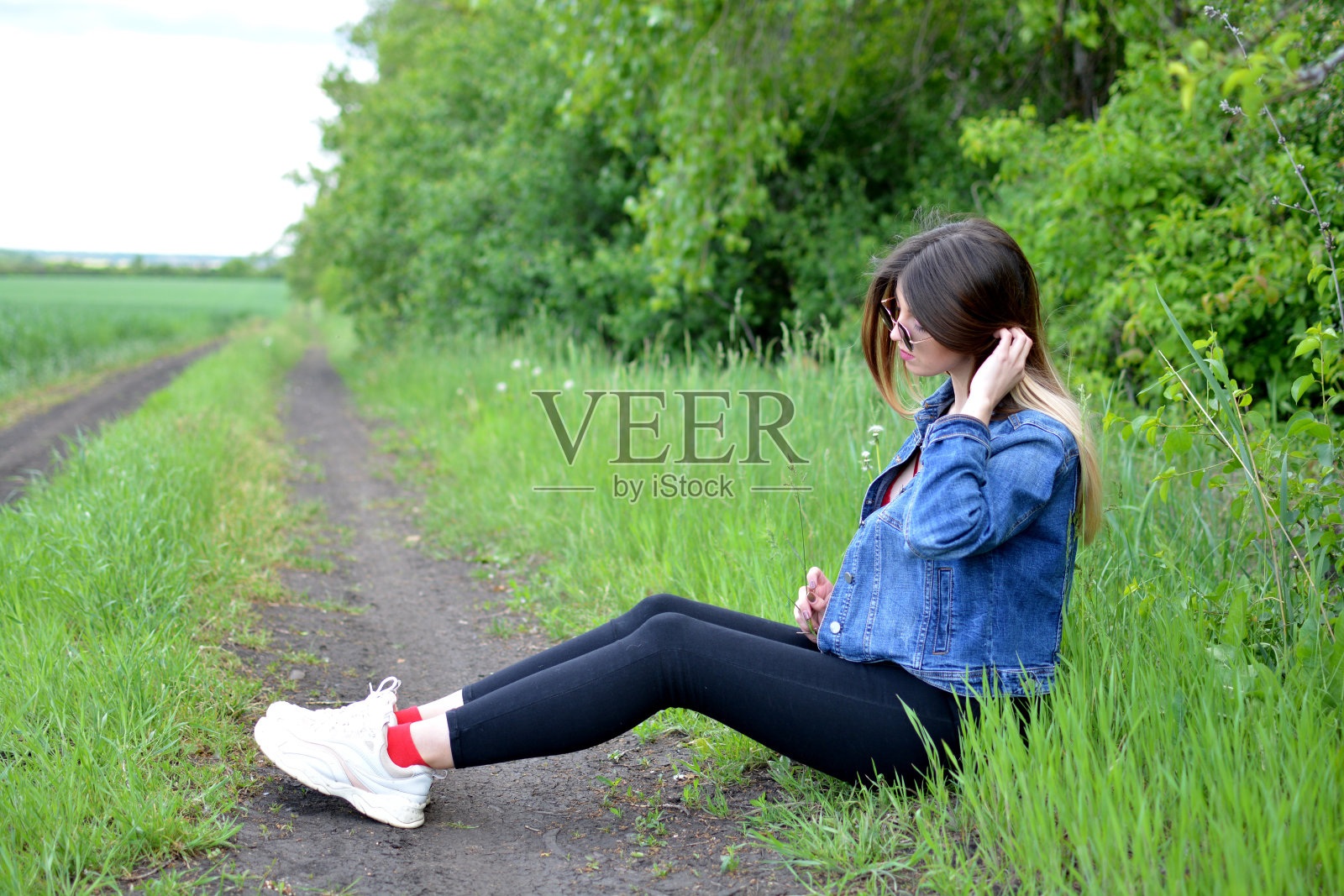 穿着牛仔裤的女孩，有着美丽的头发，脸上带着梦幻般的神情坐在路边。照片摄影图片