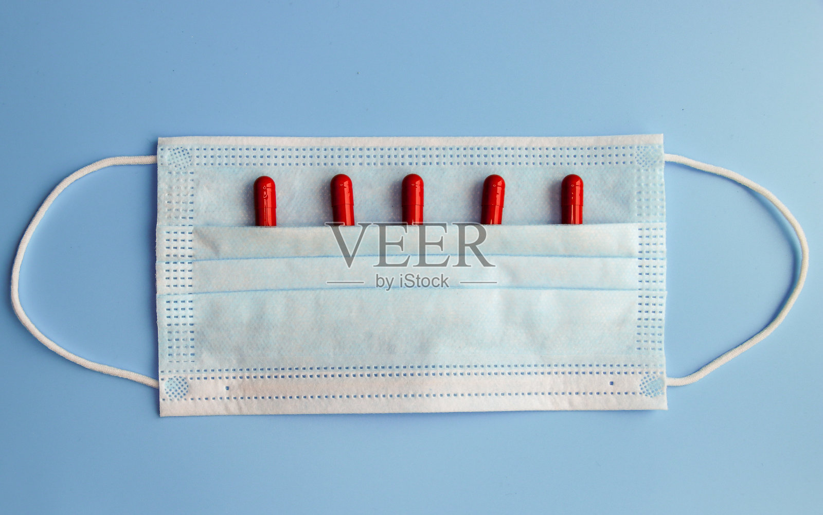 一次性防护口罩特写和草药胶囊上的蓝色背景。流感和感冒预防的概念照片摄影图片