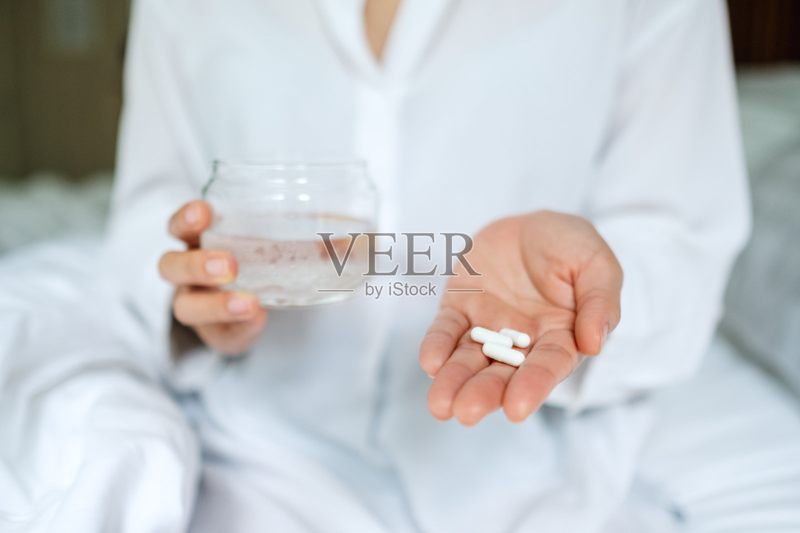 一个病人坐在床上，手里拿着白色药丸和一杯水照片摄影图片