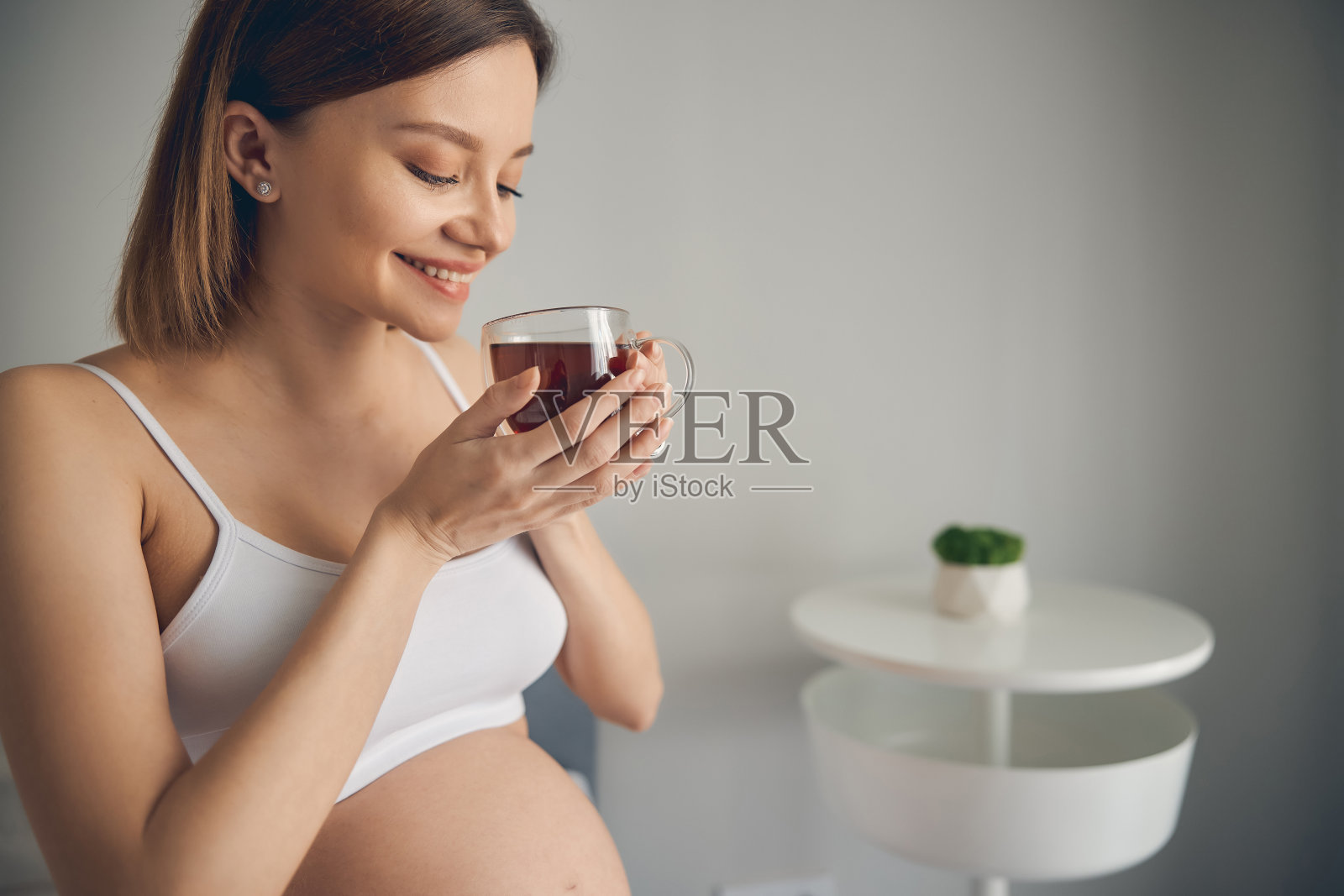 喜气洋洋的孕妇用杯在家喝茶照片摄影图片