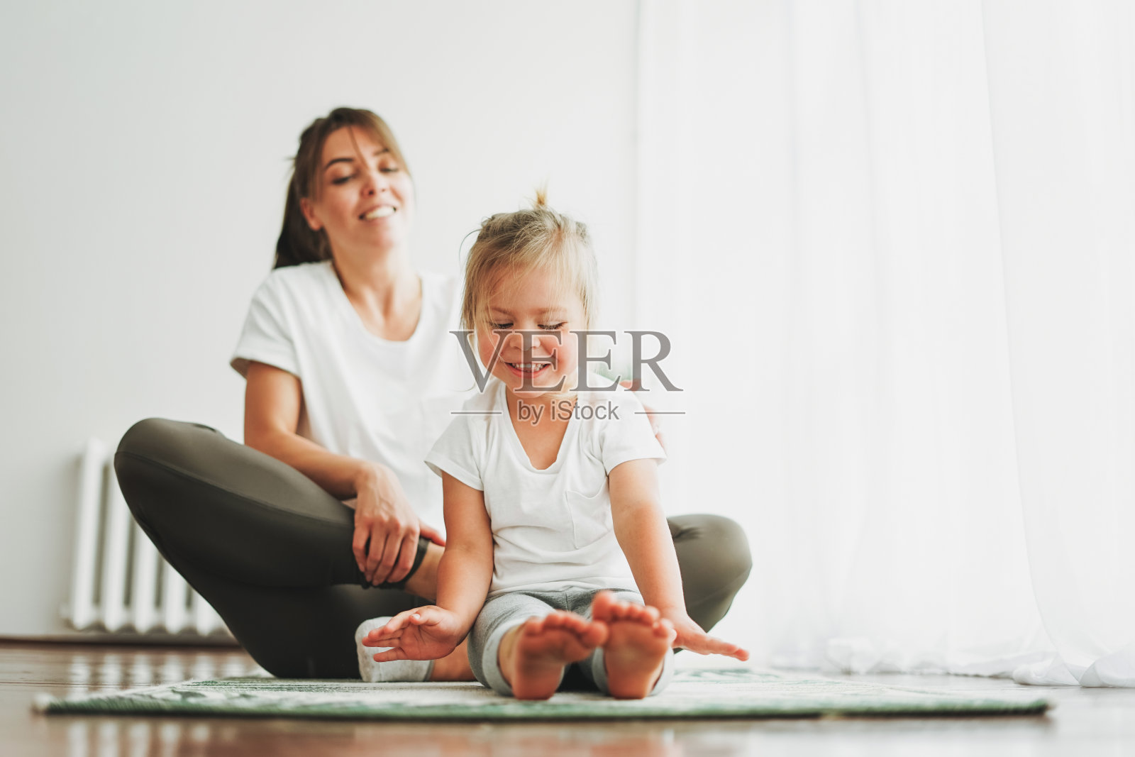 快乐的妈妈和小女儿在明亮的室内一起做瑜伽晨练照片摄影图片