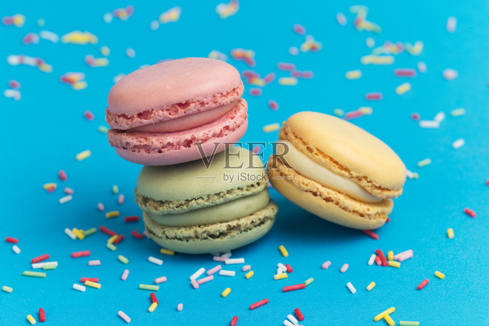 粉色，绿色和黄色的马卡龙在蓝色的背景和混合的彩色糖丝照片摄影图片
