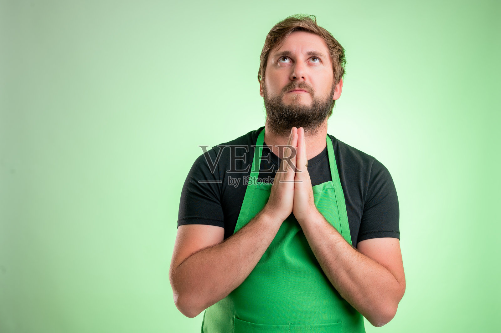 穿着绿色围裙和黑色t恤的超市员工在祈祷照片摄影图片