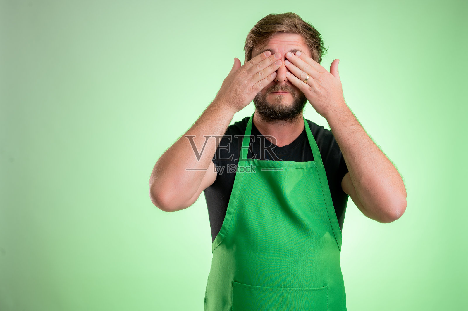 超市员工用绿色围裙和黑色t恤遮住眼睛像盲人的概念照片摄影图片