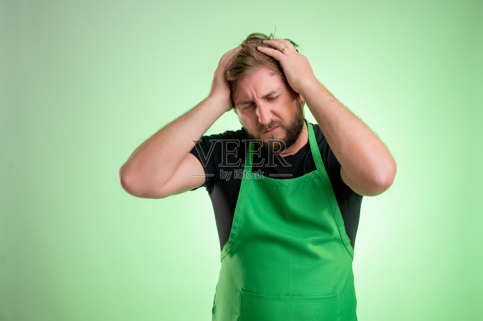 穿着绿围裙和黑t恤的超市员工头疼照片摄影图片