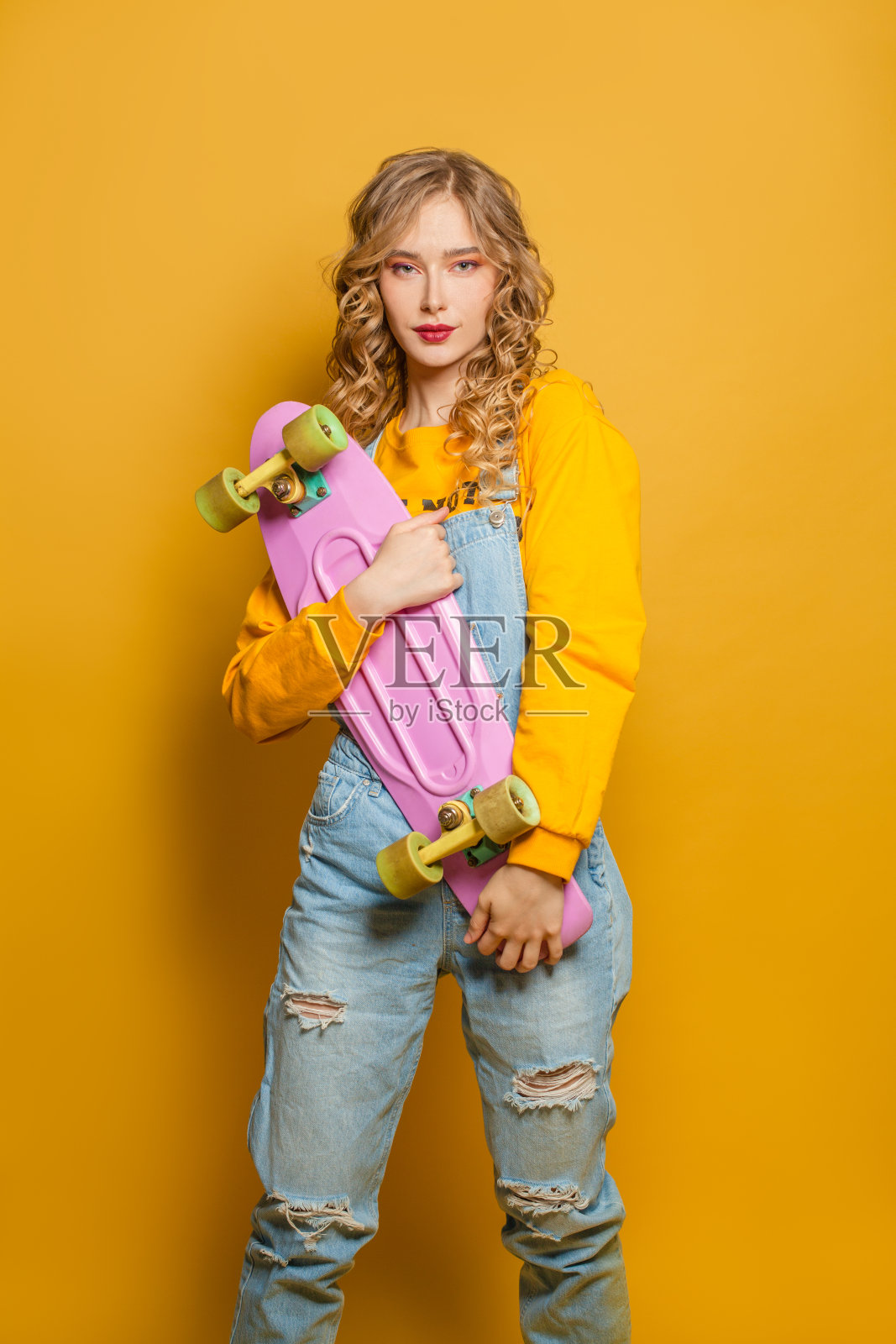 漂亮的女人在黄色运动衫拿着滑板在生动的背景照片摄影图片
