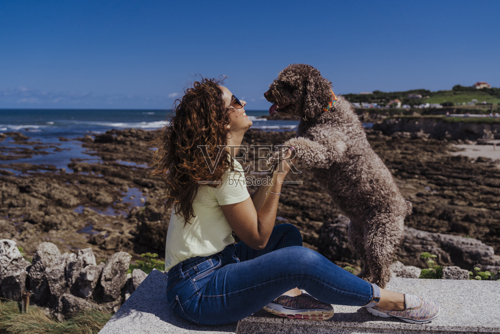 年轻女子和她可爱的西班牙水狗在户外一起享受一个阳光明媚和刮风的日子。夏季，热爱动物和假期的概念照片摄影图片