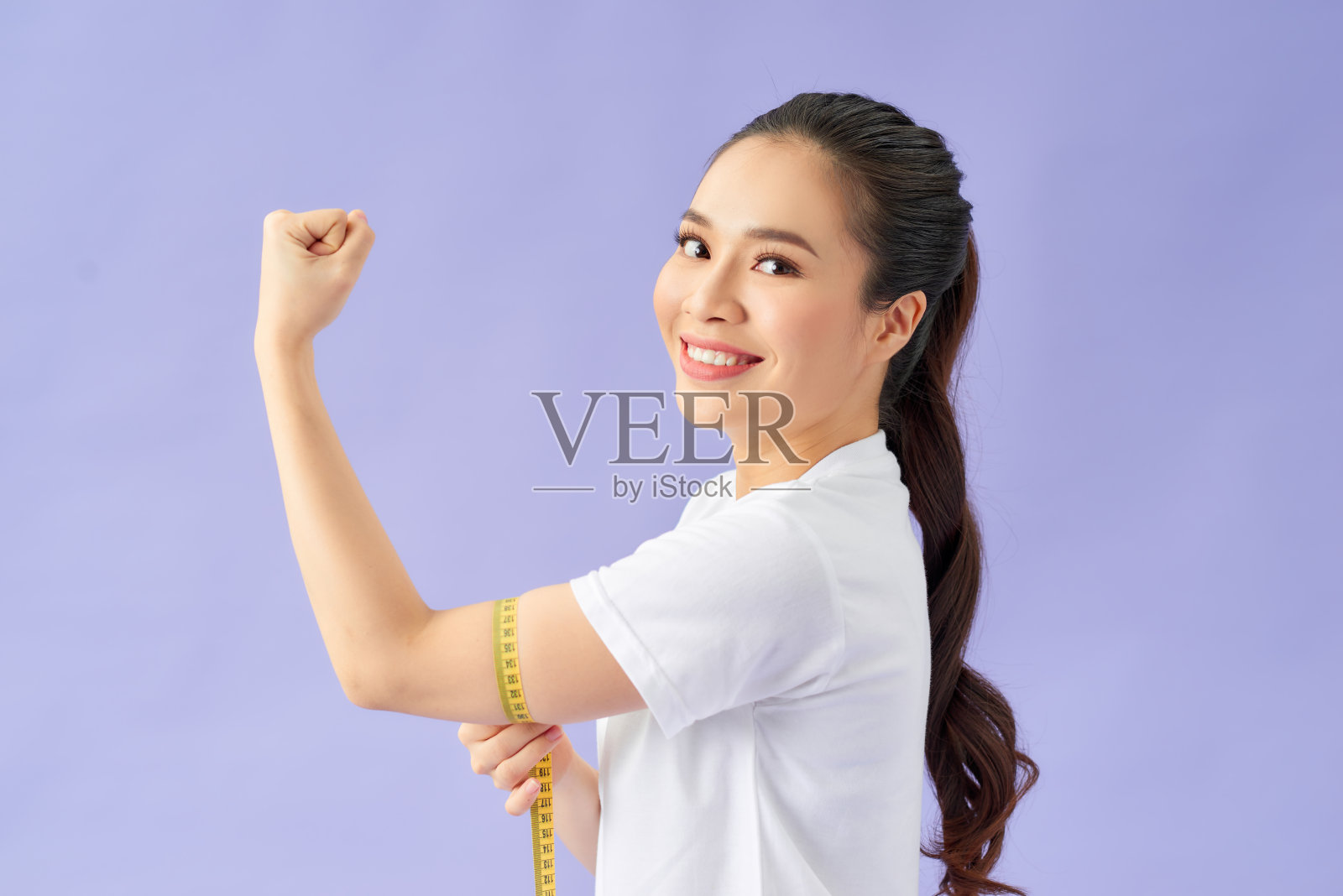 年轻的健身妇女健康女孩与测量尺测量她的二头肌孤立在紫罗兰照片摄影图片