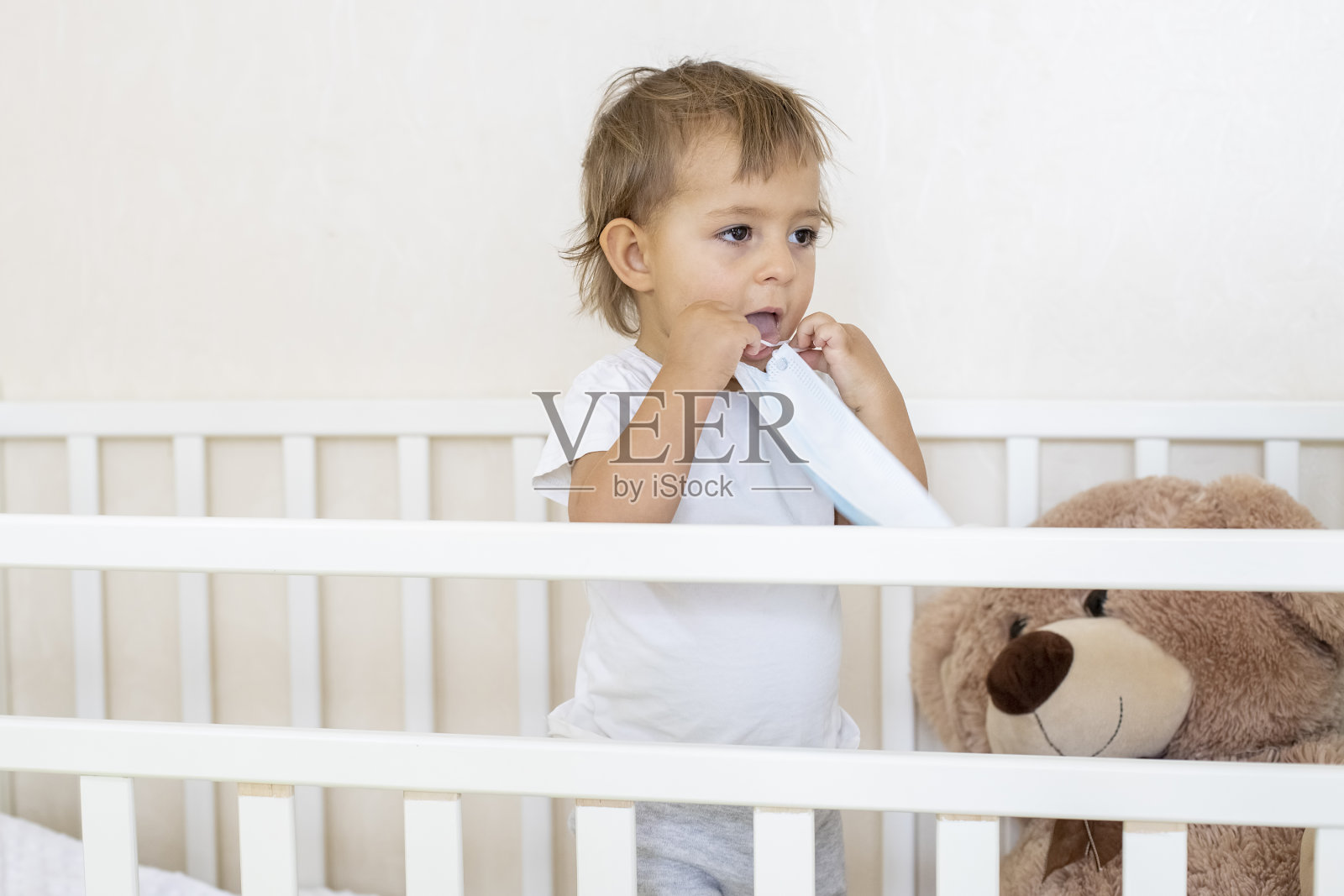 新冠病毒检疫、安全、卫生的概念。可爱的小婴儿站在婴儿床上，戴着医用口罩照片摄影图片