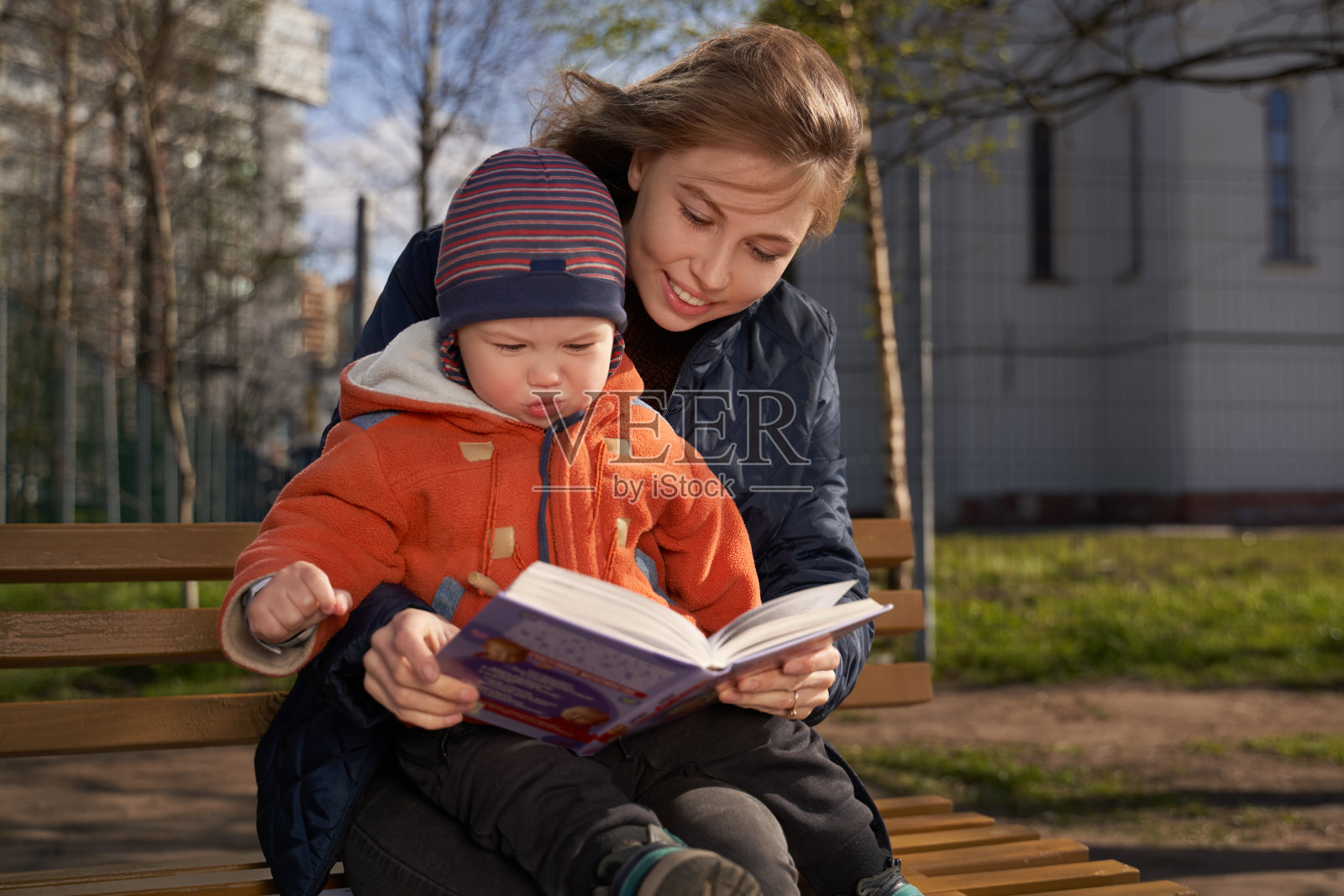 一个女孩抱着一个坐在长椅上的孩子，孩子坐在女人的腿上，看书，讲故事照片摄影图片