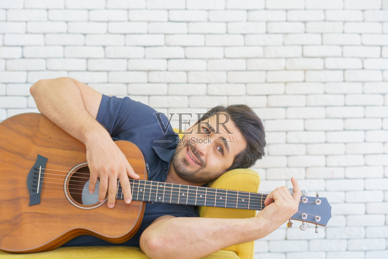 快乐的人坐在客厅的沙发上弹吉他，享受在家的悠闲时光。照片摄影图片