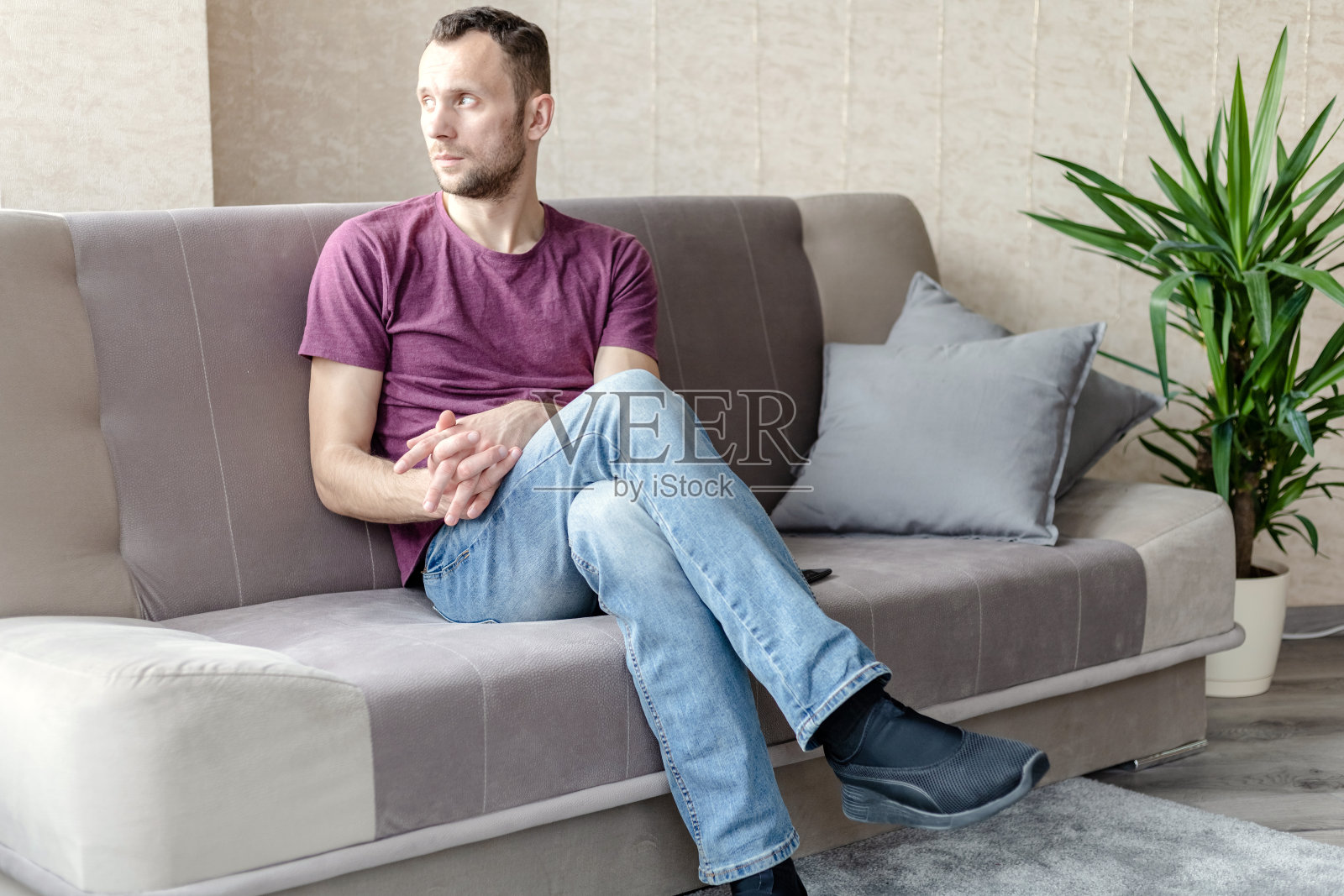 一个平静的年轻人坐在一个明亮的房间里的沙发上望着窗外照片摄影图片