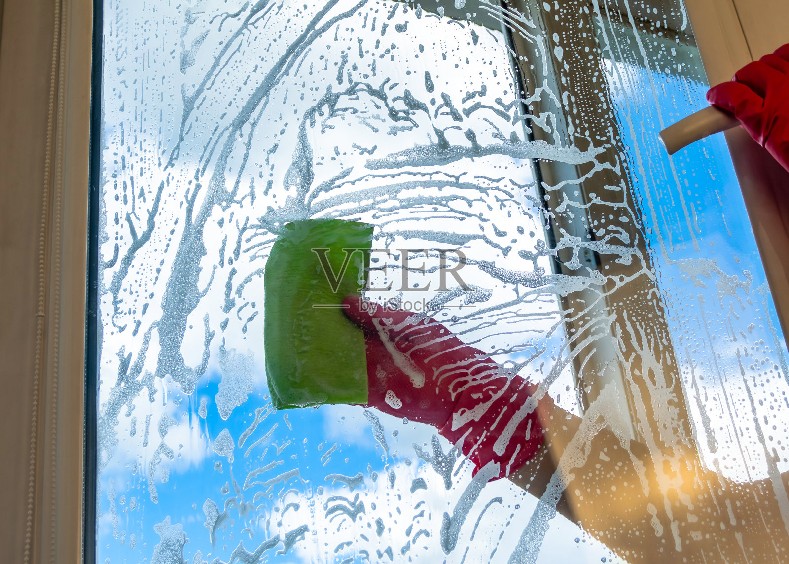 洗窗户。玻璃上涂了大量的肥皂泡沫。一个戴着粉红色橡胶手套的清洁工用一块绿色的抹布擦窗户照片摄影图片