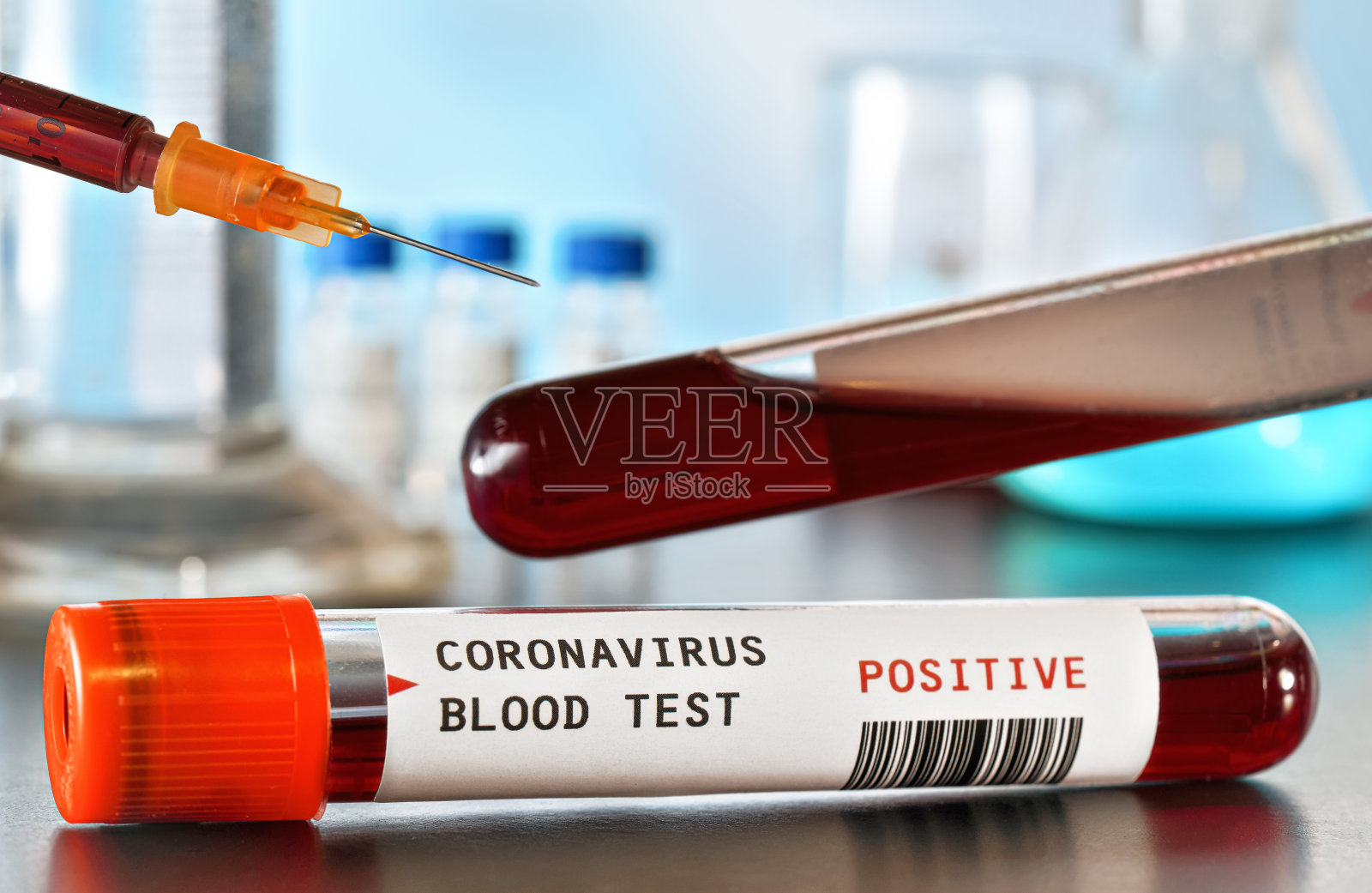 带血的样本瓶，标签上写冠状病毒检测，阳性，上面是皮下注射器针头。模糊的实验室设备背景。疫情期间的Covid-19检测概念照片摄影图片