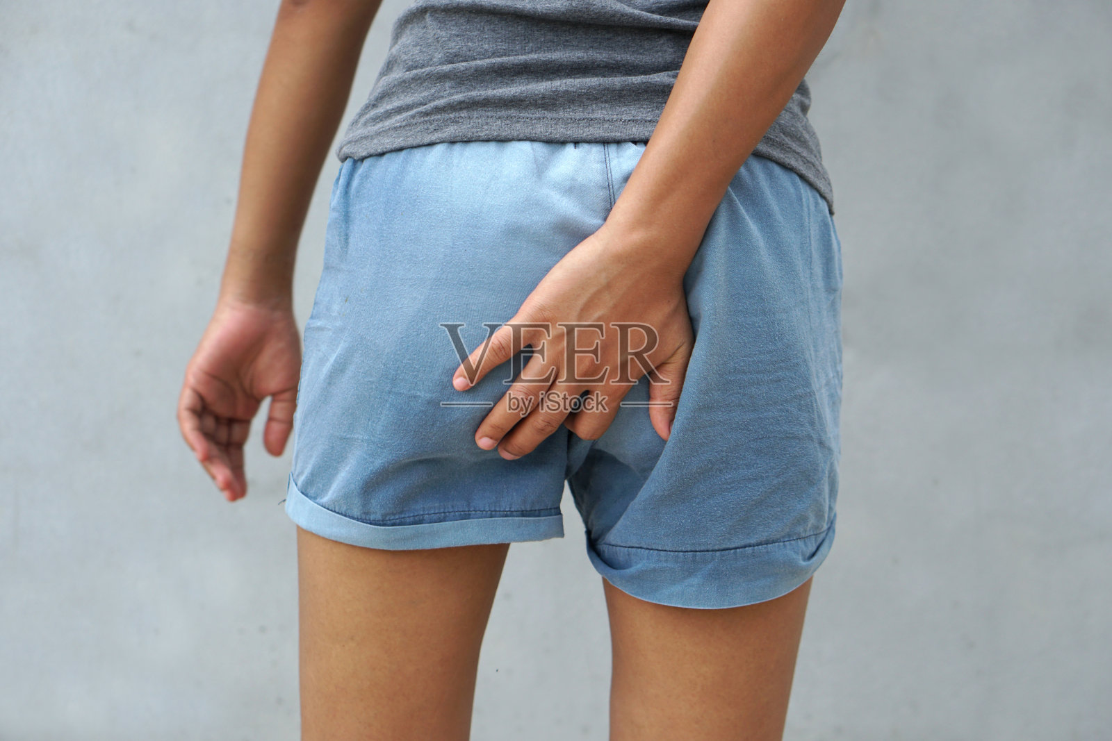 穿着灰色衣服的女人搔痒，搔大腿部位照片摄影图片