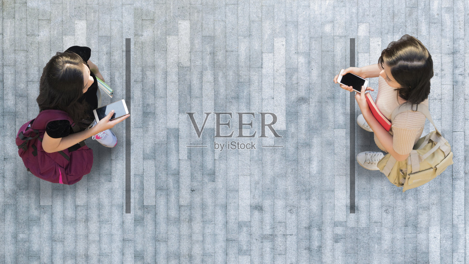 社会距离中的人类生活。两名女学生用智能手机拍摄的鸟瞰图，站在灰色的人行道上，路面上空无一人。照片摄影图片