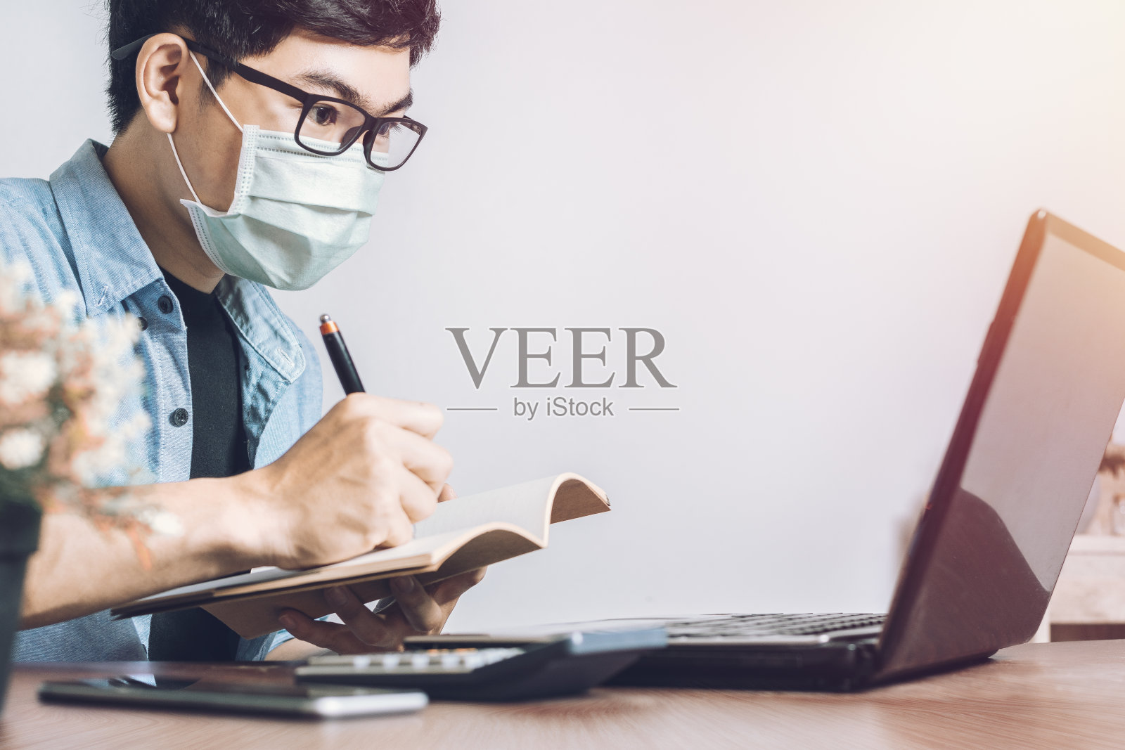 亚洲男子戴口罩以预防冠状病毒。使用笔记本电脑在家里工作。照片摄影图片