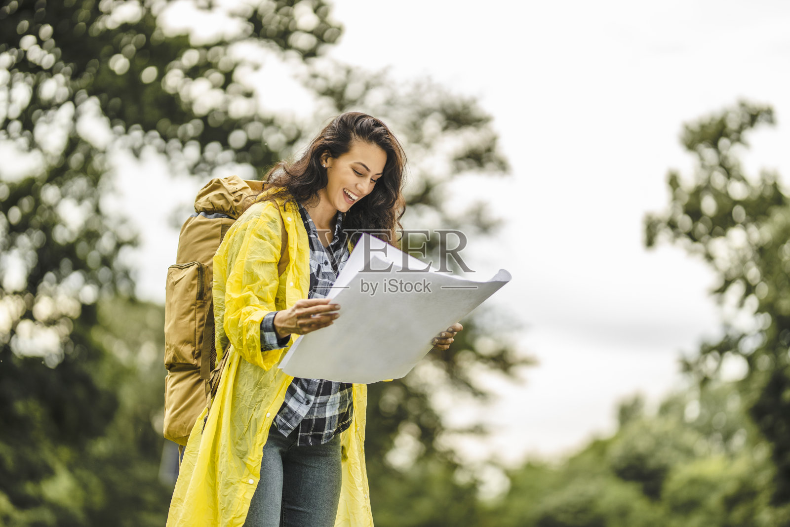 年轻女子穿着防水夹克，看地图，在雨中徒步旅行照片摄影图片
