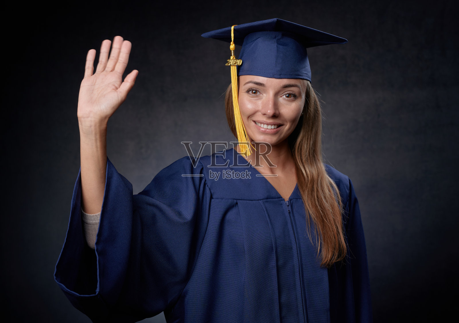 微笑的年轻女子挥舞着手，戴着蓝色的帽子和长袍照片摄影图片