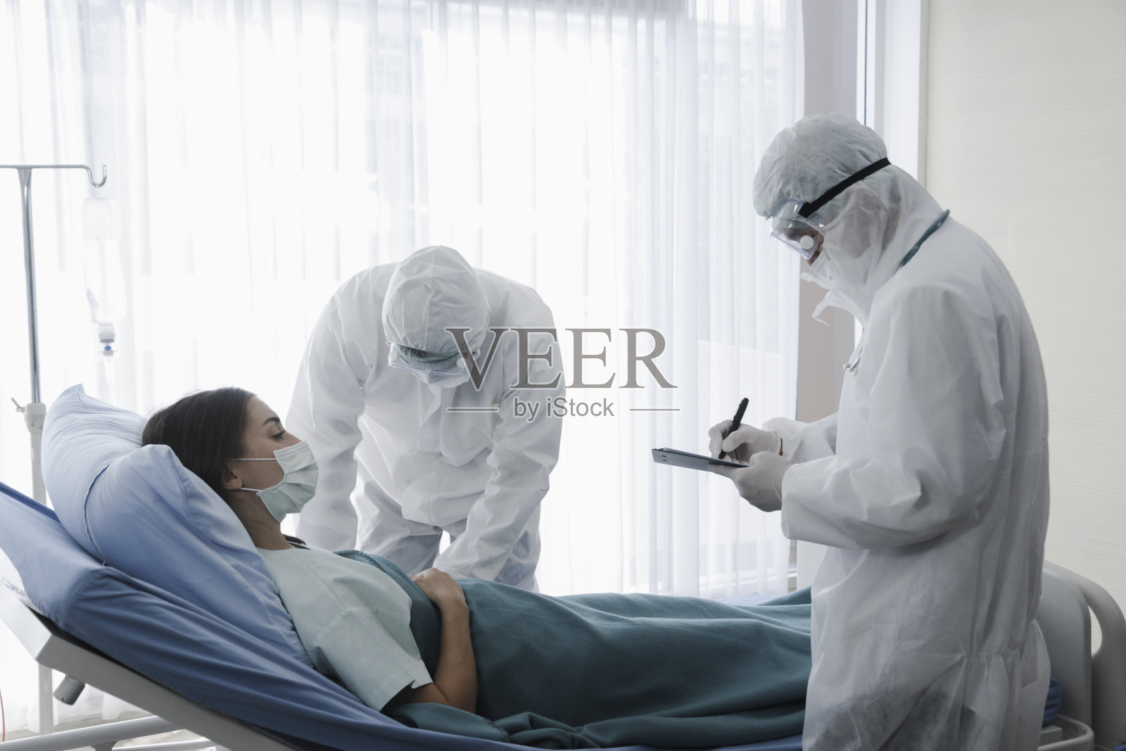 疾病治疗室为感染病人，感染病人女子躺在病床上，医生穿着防护服在医院隔离，照顾病人照片摄影图片
