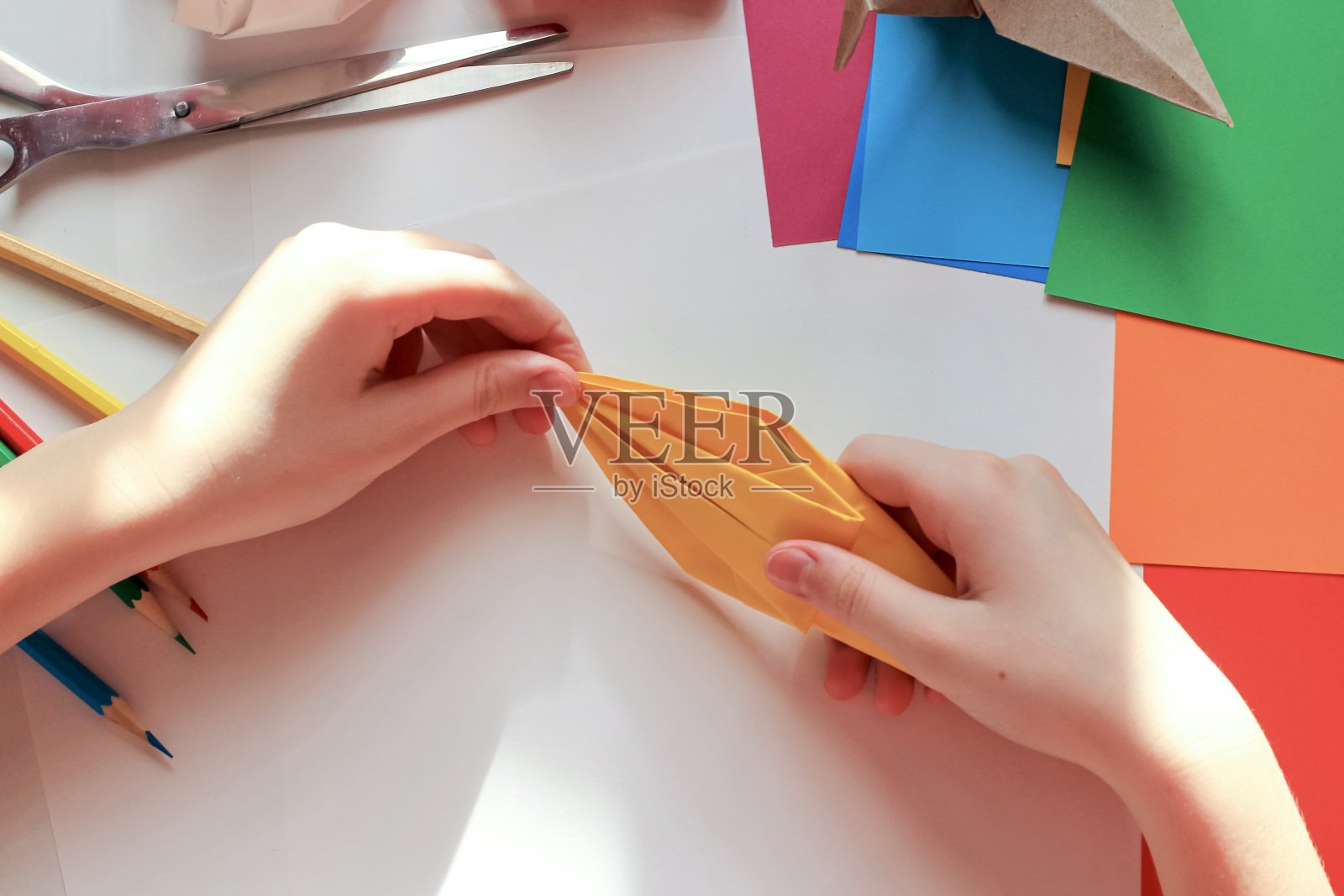 孩子们的手在白色的背景上用黄色的纸做折纸鹤。一步一步的折纸教程。孩子的创意观念，回到学校。照片摄影图片